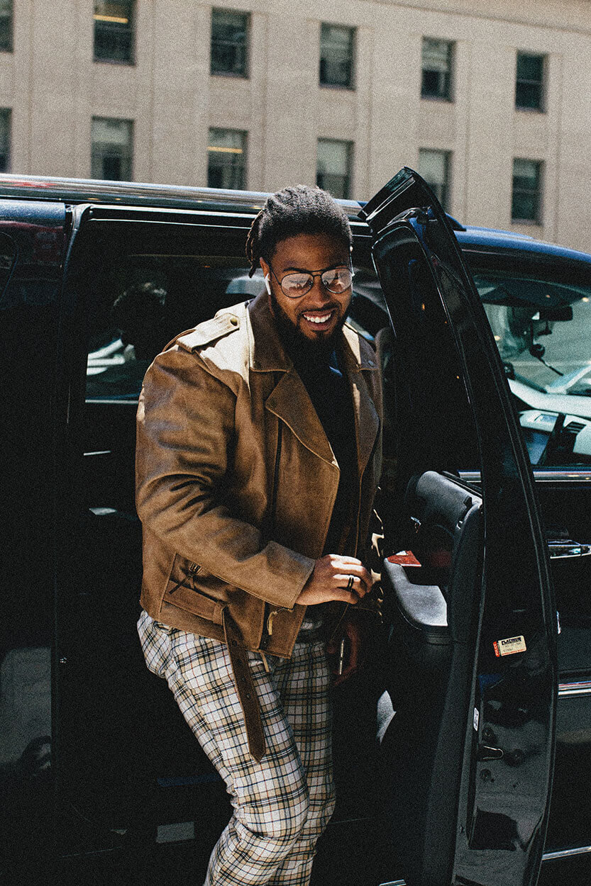 Corey in a brown jacket stepping out of a car